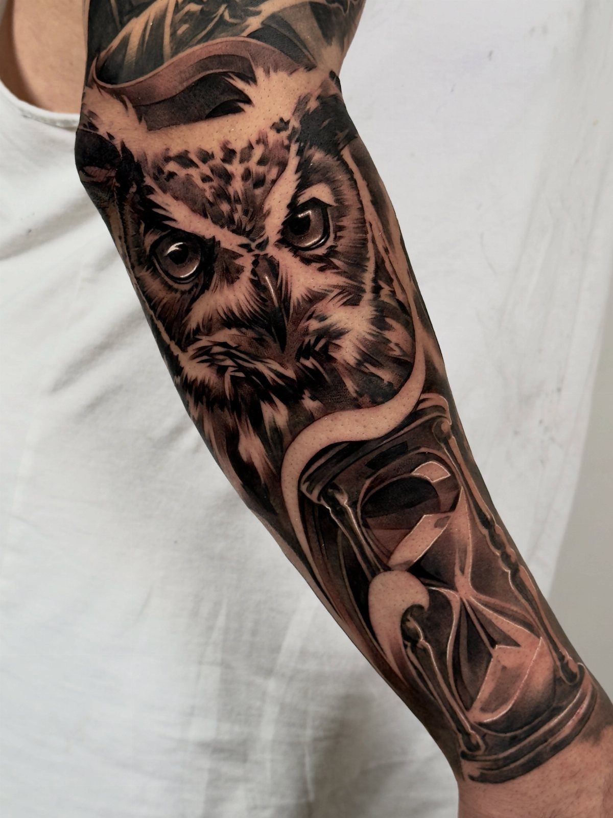 Hour Glass Tattoo Ideas: 12 Designs for Every Style 9 A detailed black and grey realism tattoo of an owl and an hourglass on a forearm.