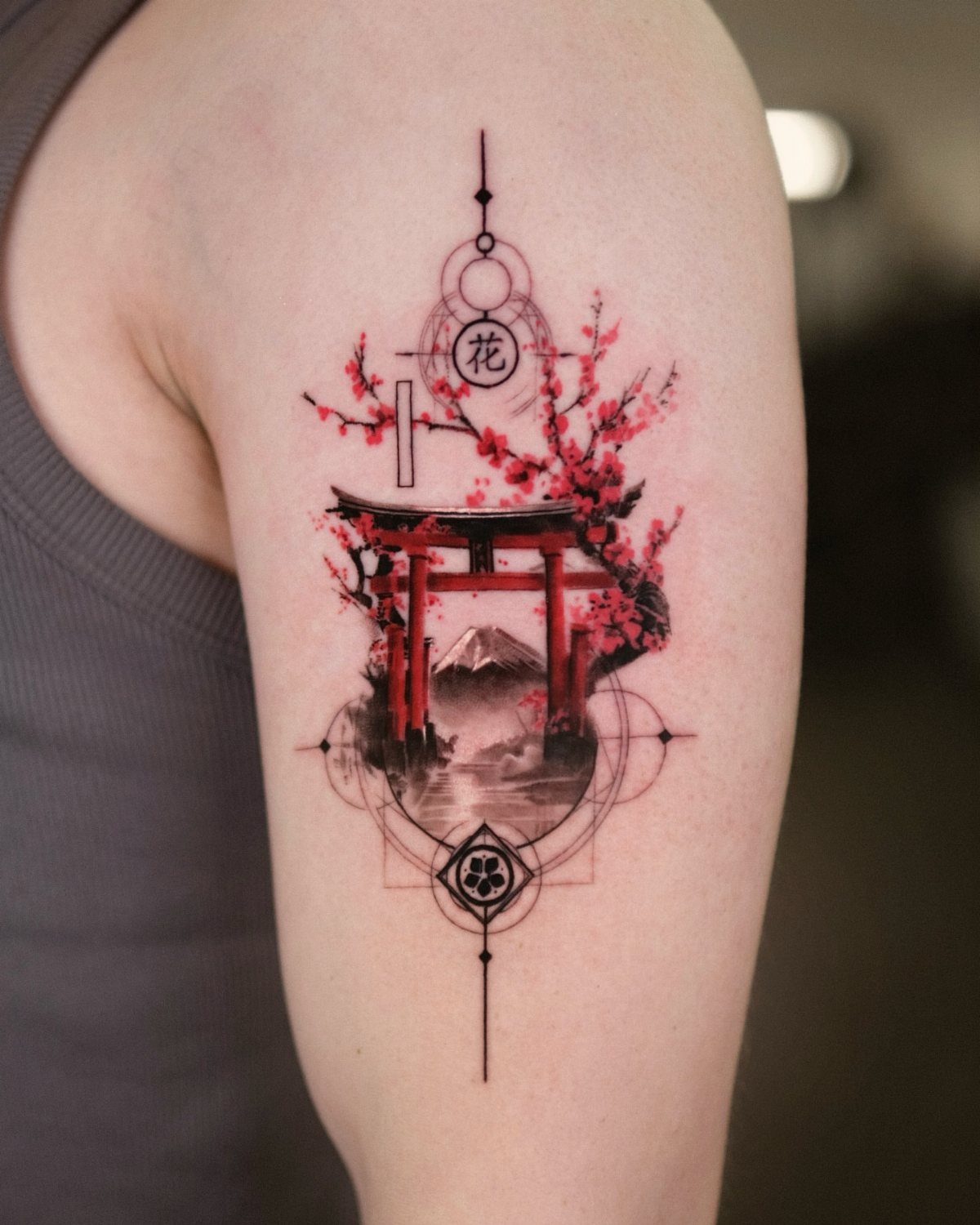 A detailed tattoo on an arm showing a red torii gate and pink cherry blossoms.