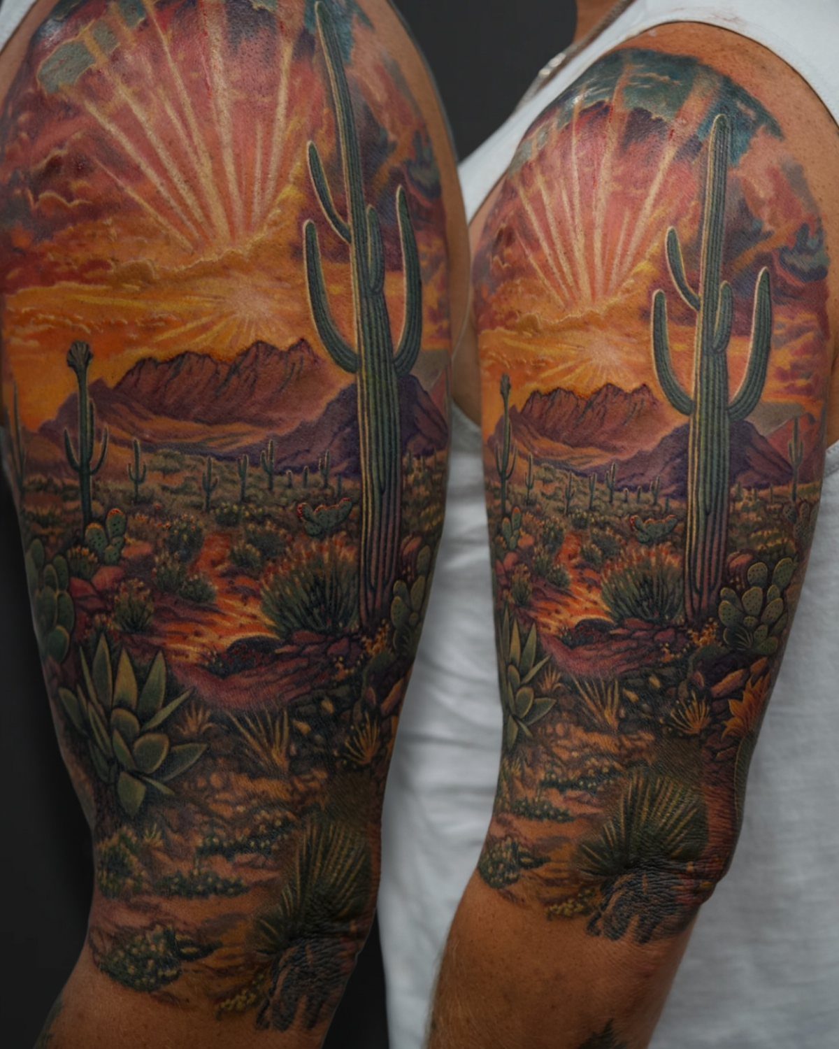 A colorful tattoo on an arm showing a desert landscape with cacti and a sunset.