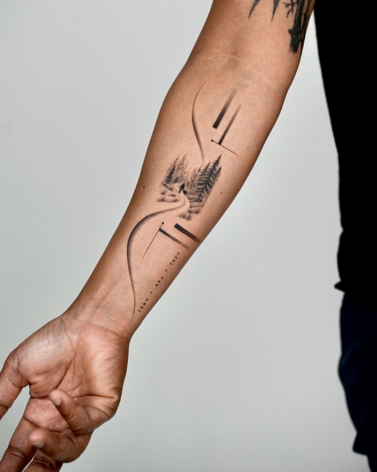 A minimalist landscape tattoo on a person's forearm featuring trees and geometric lines.