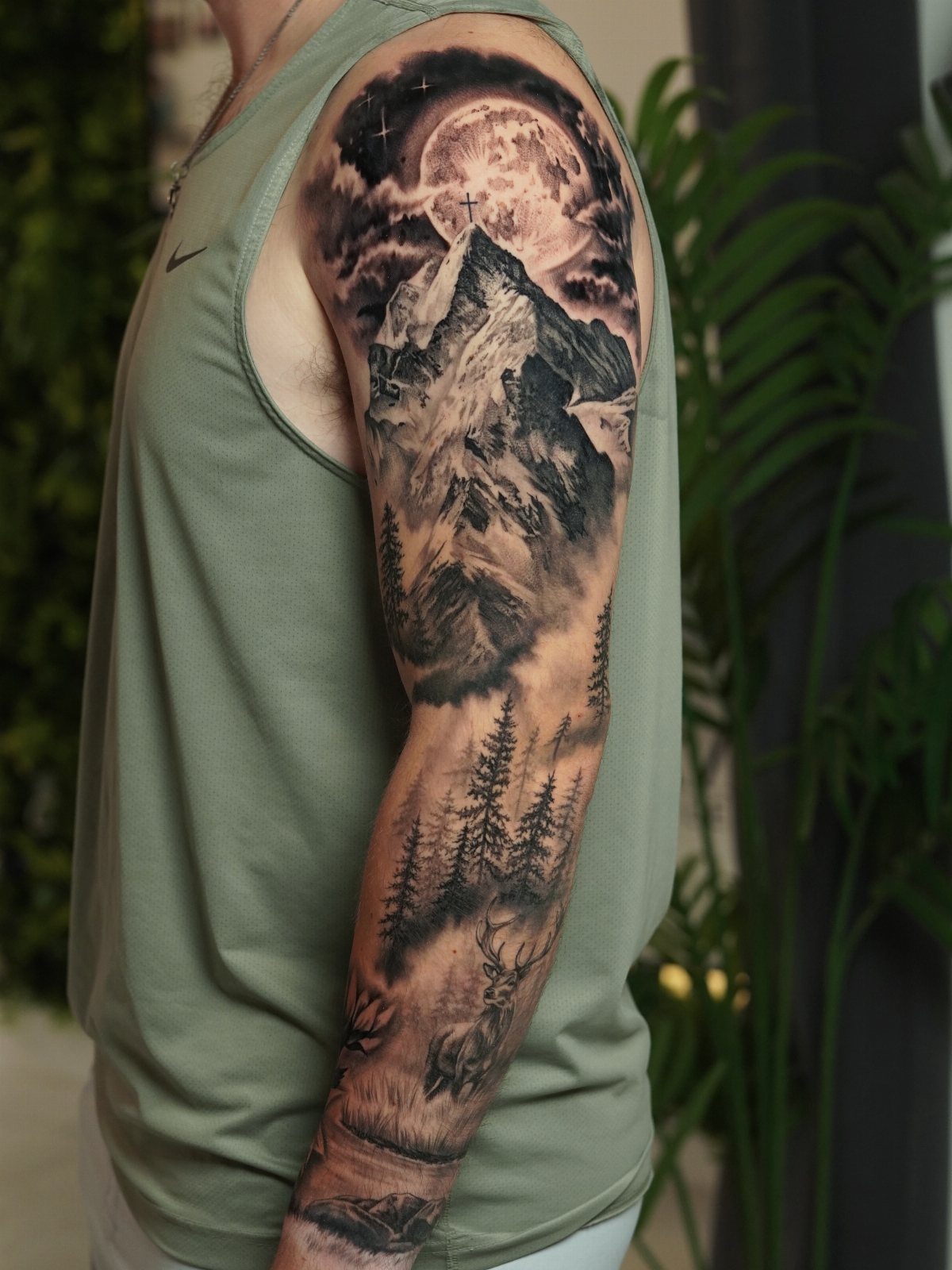 7 Landscape Tattoo Sleeve Ideas for Your Next Ink 1 A detailed black and grey tattoo sleeve depicting mountains, a moon, and a forest on an arm.