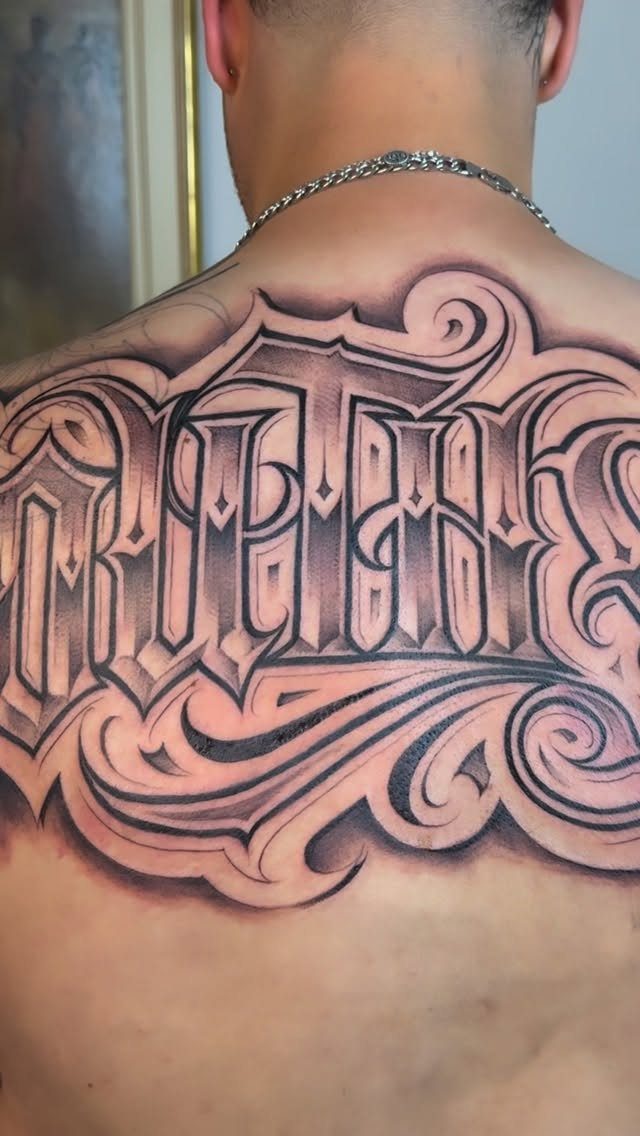 Large Back Script Tattoo: 5 Styles That Fill the Space 5 Large black and grey ornamental script tattoo covering a person's upper back and shoulders.