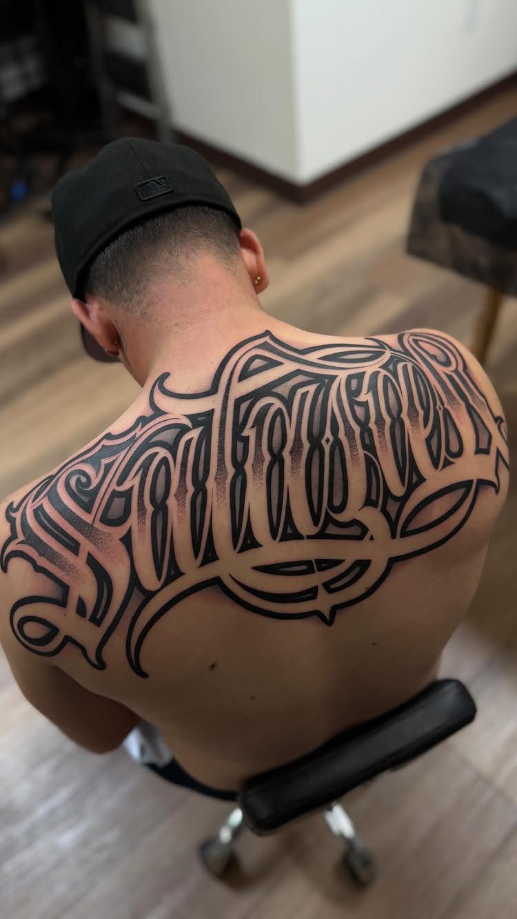 Large Back Script Tattoo: 5 Styles That Fill the Space 4 A large black and grey gothic script tattoo covering a person's upper back.
