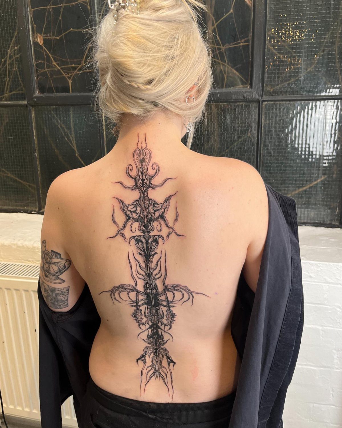 Large Back Script Tattoo: 5 Styles That Fill the Space 3 A person with blonde hair displaying a large, black ornamental tattoo running down their spine.