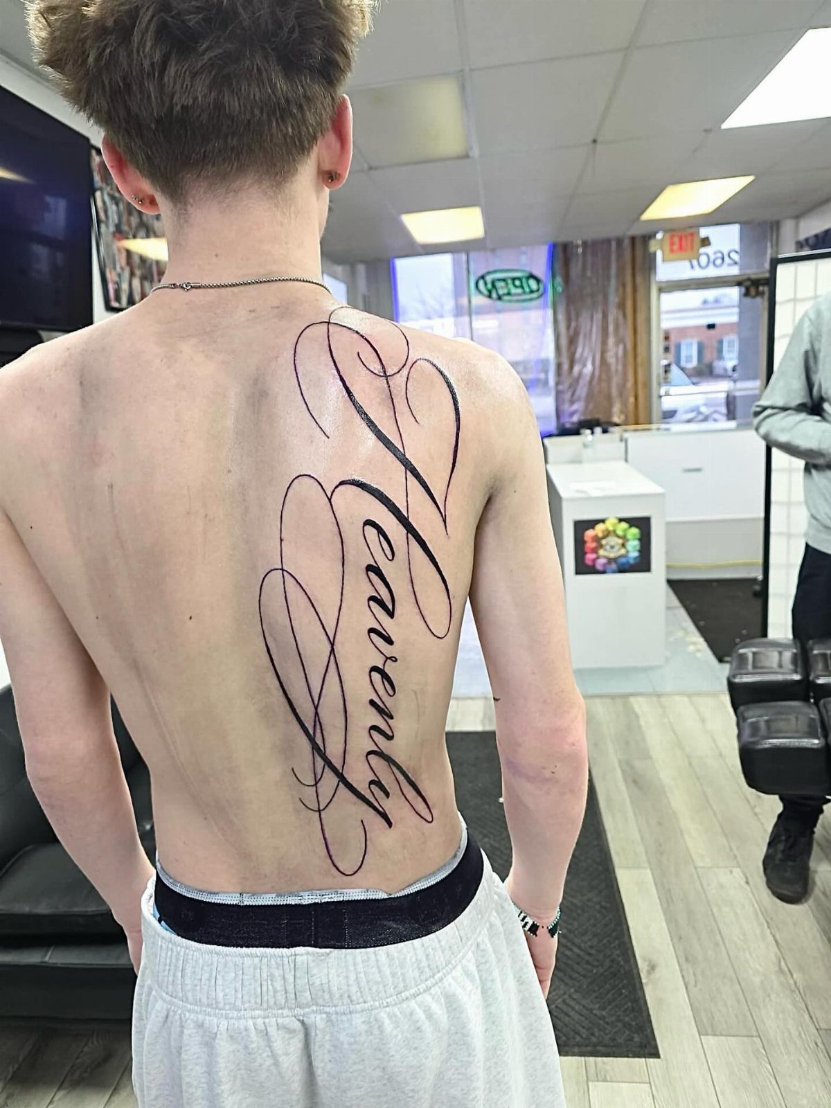 Large Back Script Tattoo: 5 Styles That Fill the Space 1 A man's back showing a large vertical script tattoo of the word Heavenly in black ink.