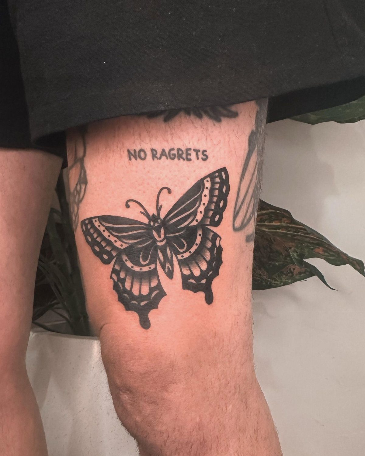 Man Leg Tattoo: 8 Styles That Fill the Canvas From Hip to Ankle 3 A black traditional butterfly tattoo with decorative patterns on a person's leg.