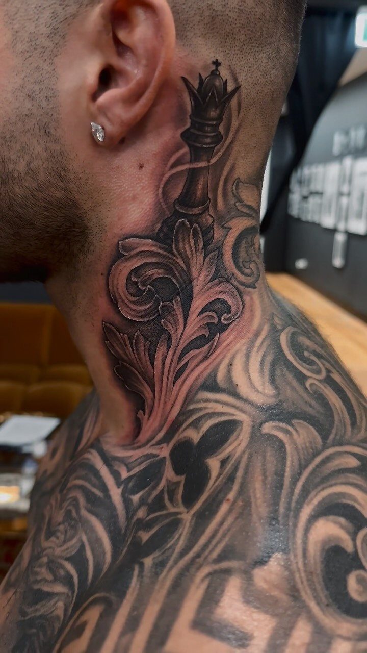 A man's neck featuring a large black and grey chess king filigree tattoo.