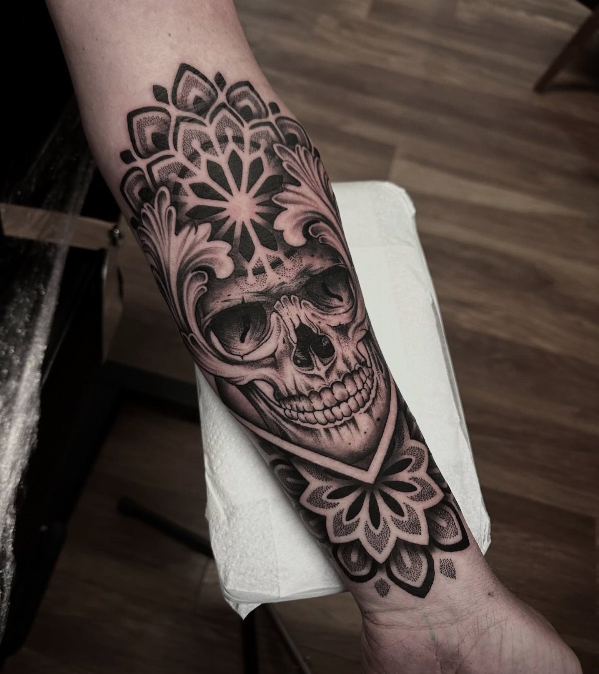 A detailed black and grey skull tattoo with ornate filigree patterns on a person's forearm.