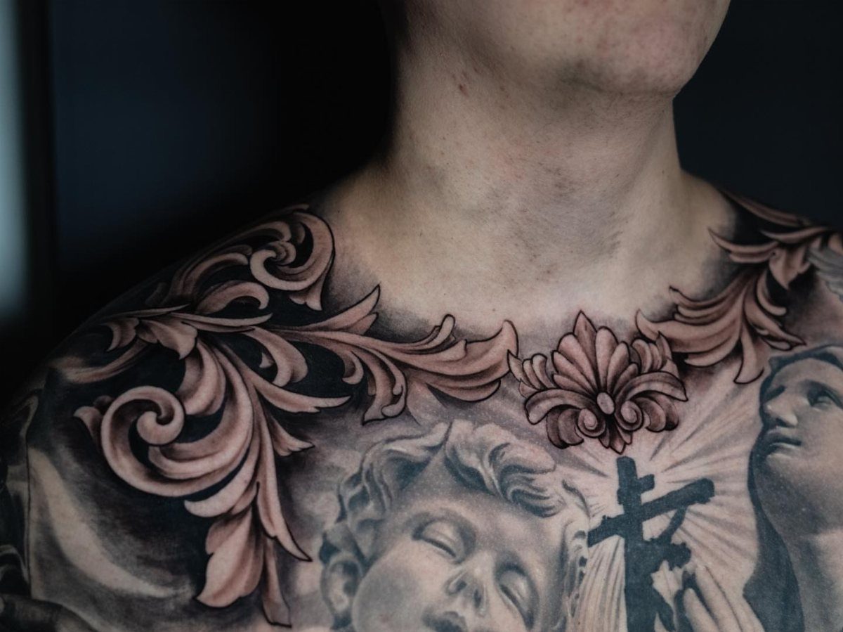 Intricate black and grey filigree tattoo design covering a man's upper chest and collarbone area.