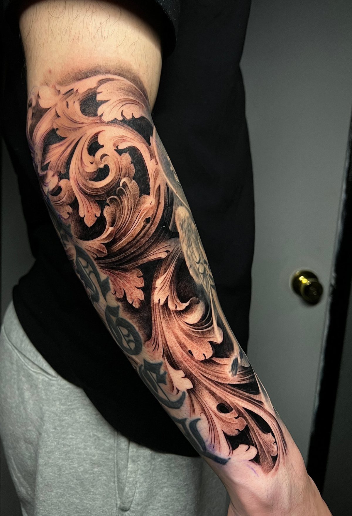 Intricate black and grey acanthus leaf tattoo covering a person's forearm with swirling, ornate patterns.