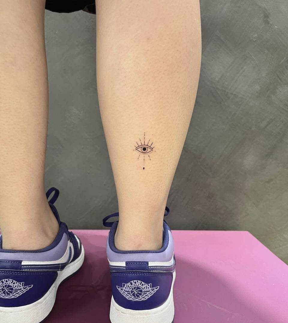 14 Minimalist Tattoo Design Ideas That Stay Simple and Clean 10 A minimalist black ink evil eye tattoo on a person's lower leg above the ankle.