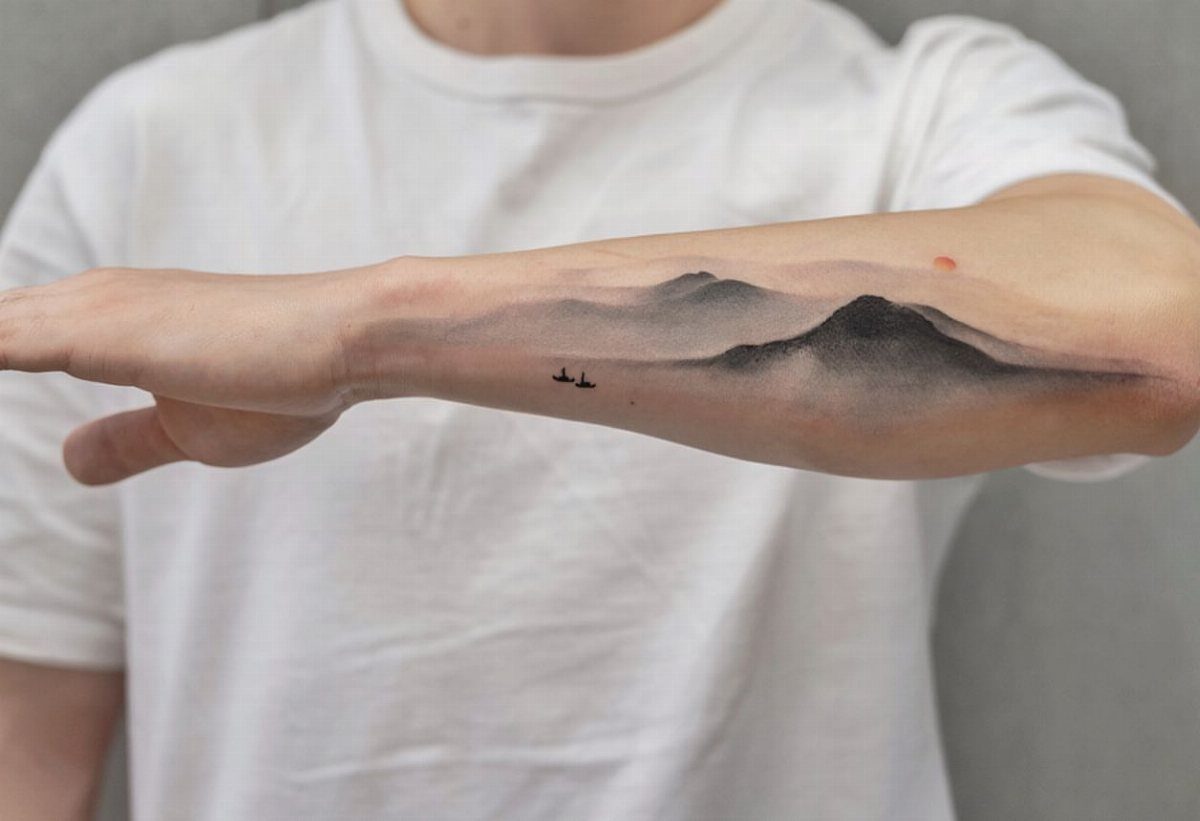 14 Minimalist Tattoo Design Ideas That Stay Simple and Clean 4 A forearm tattoo depicting a misty mountain landscape with small birds in flight.