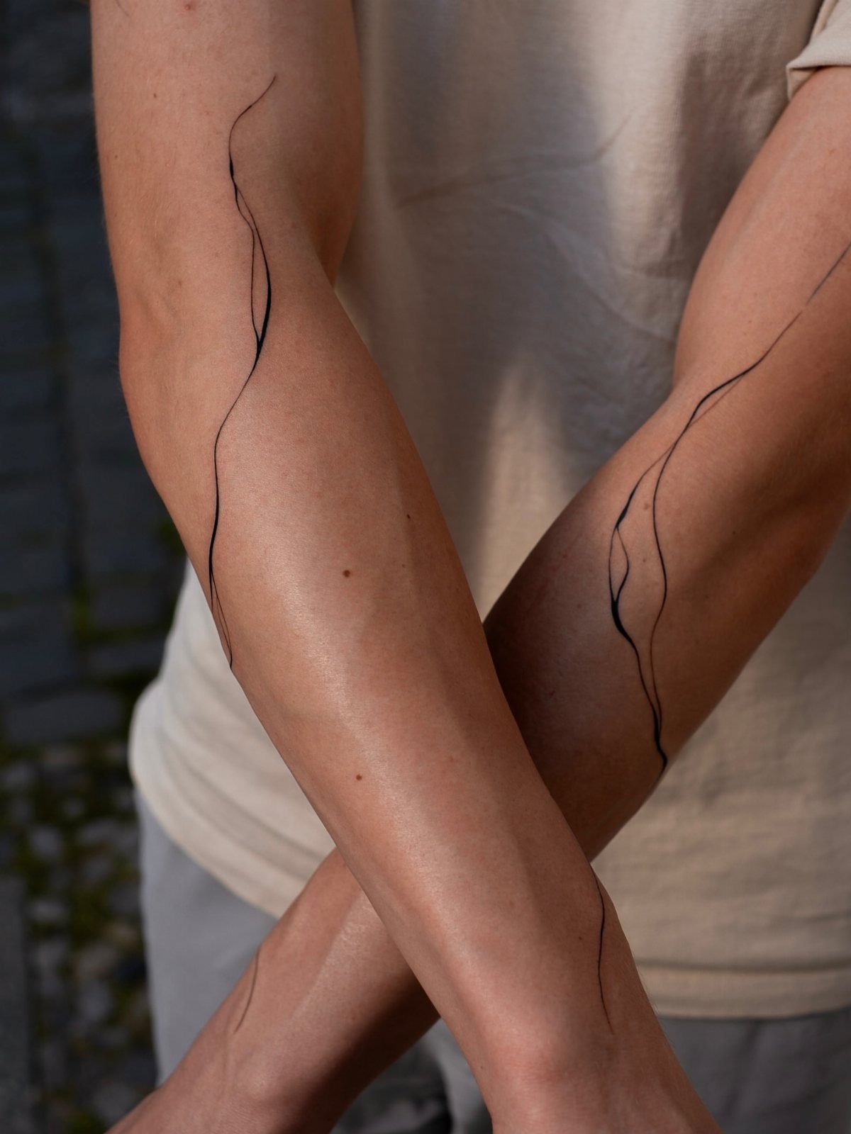 14 Minimalist Tattoo Design Ideas That Stay Simple and Clean 7 A person's arms with a single continuous line minimalist tattoo flowing along the skin.