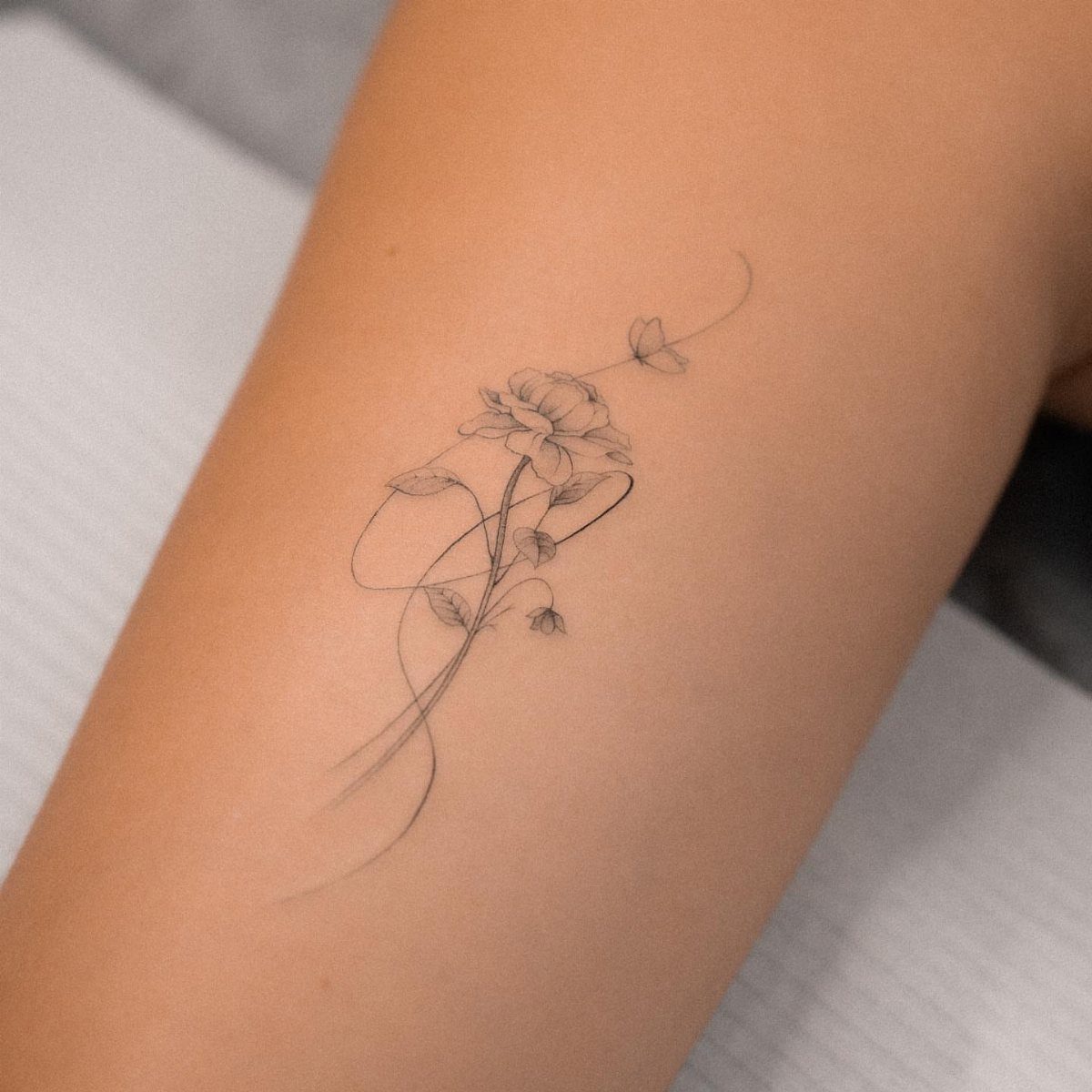 14 Minimalist Tattoo Design Ideas That Stay Simple and Clean 3 A delicate fine line floral tattoo with swirling stems on a person's arm.
