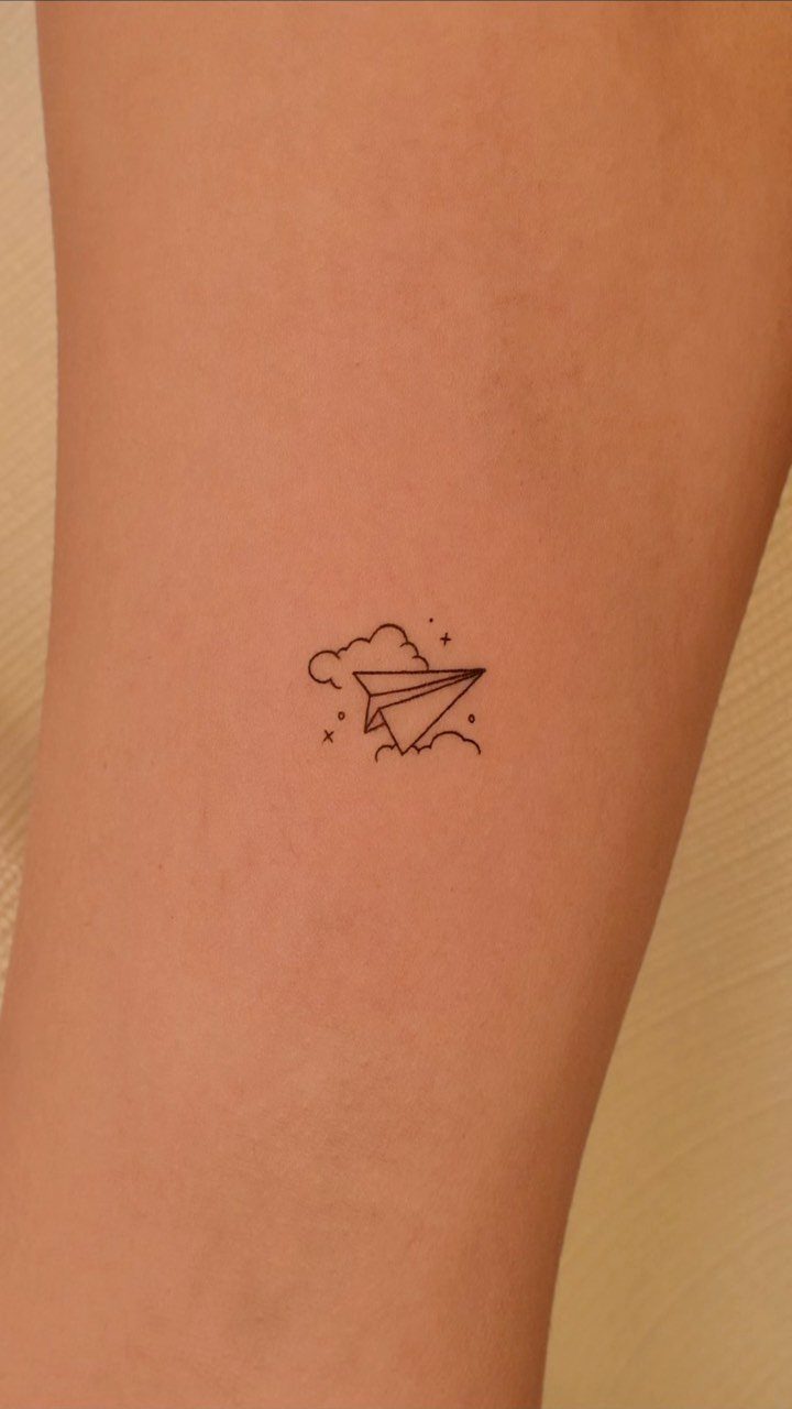 14 Minimalist Tattoo Design Ideas That Stay Simple and Clean 5 A tiny minimalist paper airplane tattoo with a small cloud and stars on skin.