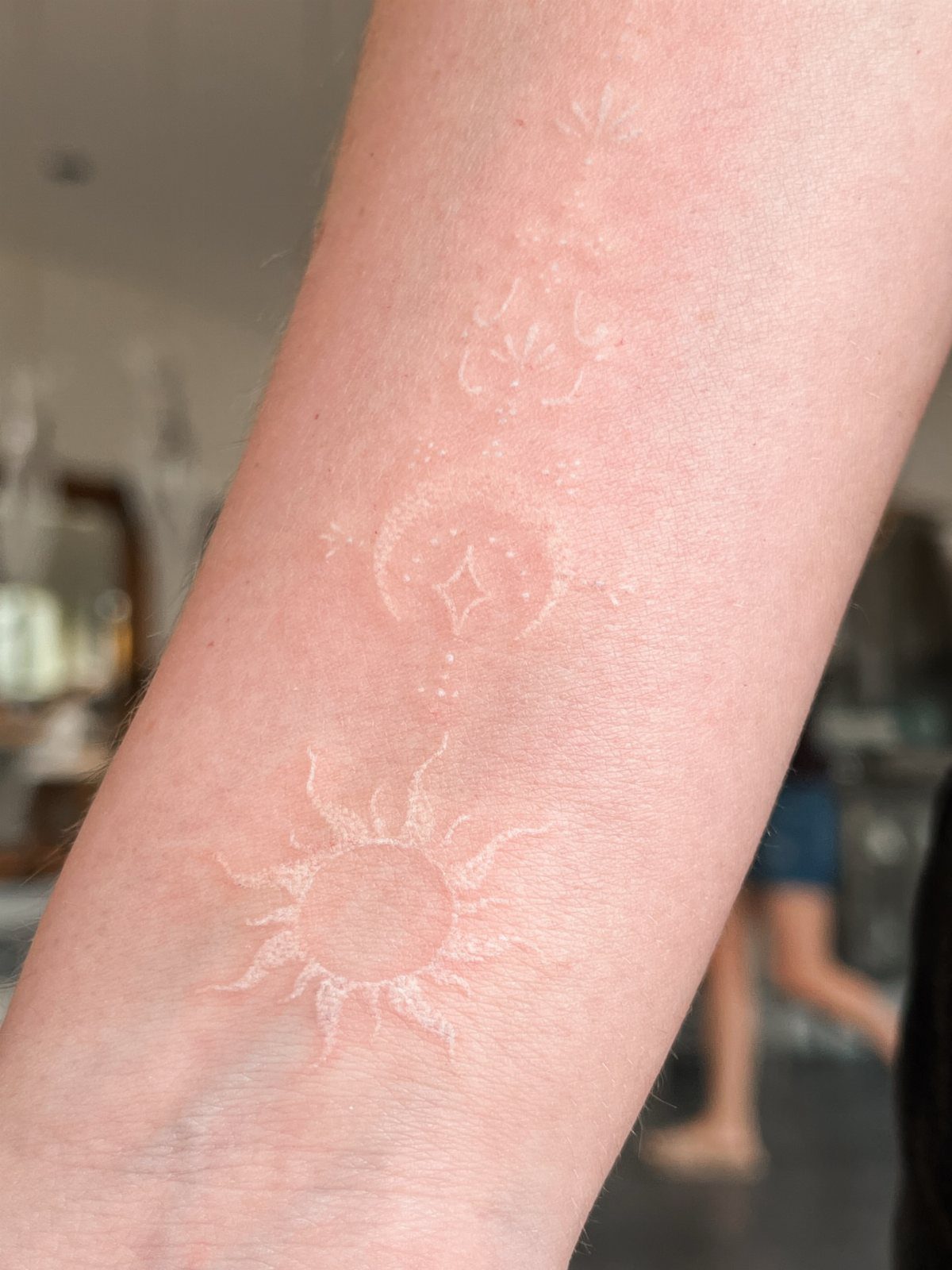 14 Minimalist Tattoo Design Ideas That Stay Simple and Clean 8 White ink tattoos of a sun, moon, and stars on a person's forearm.