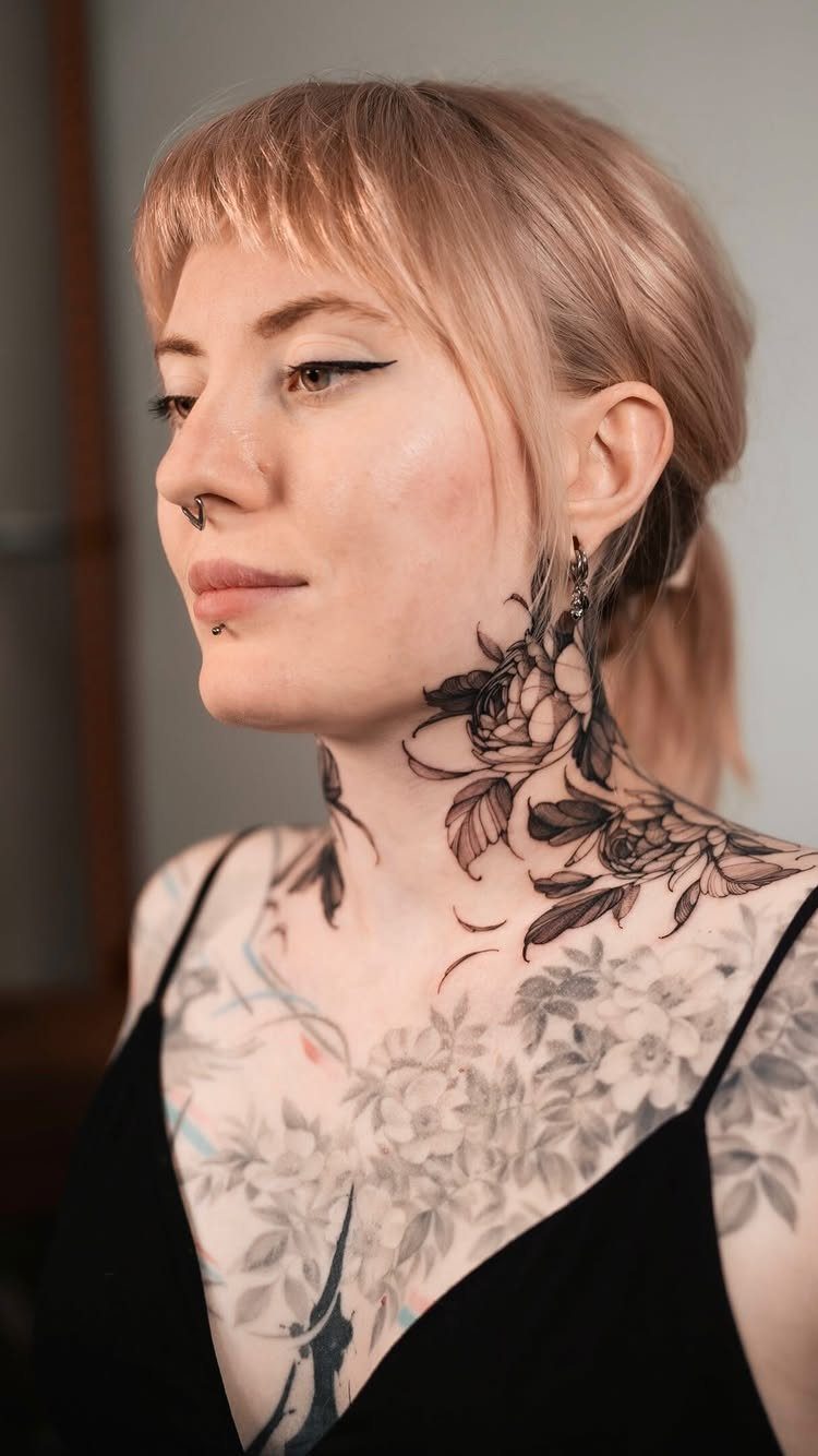 7 Neck Tattoo Designs for Women That Actually Fit the Narrow Canvas 1 A woman with blonde hair displaying a large black floral tattoo on her neck and shoulder.