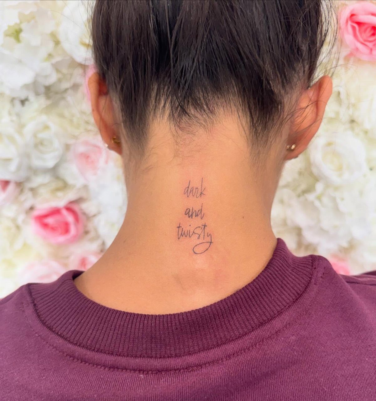 Script Tattoo Placement: 9 Positions That Work 9 A person's neck featuring a small script tattoo reading dark and twisty against a floral background.