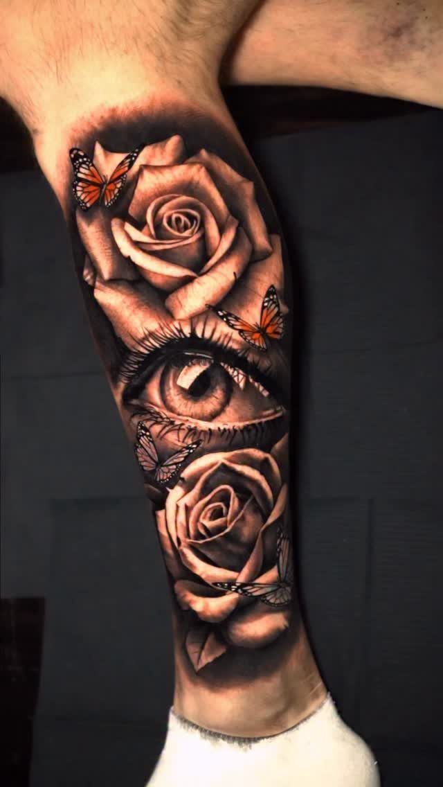 Sick Tattoo Art: 9 Styles That Redefine the Needle 9 A detailed black and grey tattoo of an eye surrounded by roses and butterflies on a leg.