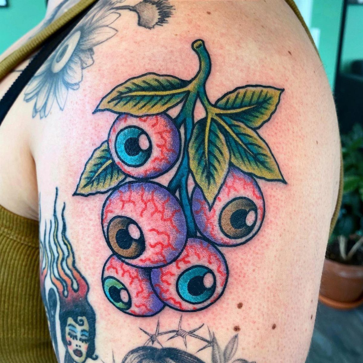 Sick Tattoo Art: 9 Styles That Redefine the Needle 8 A colorful tattoo of five eyeballs hanging from a green leafy stem on a person's shoulder.