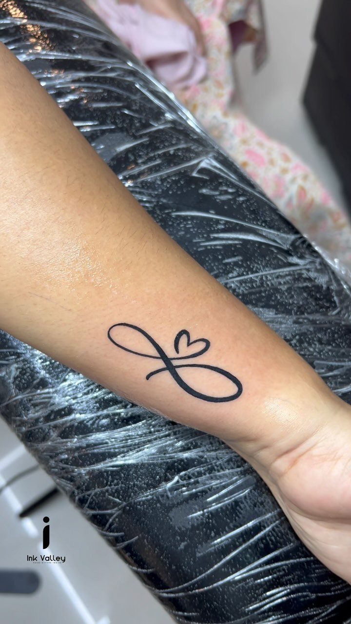 Sick Tattoo Art: 9 Styles That Redefine the Needle 6 An infinity symbol tattoo with a small heart design on a person's forearm.
