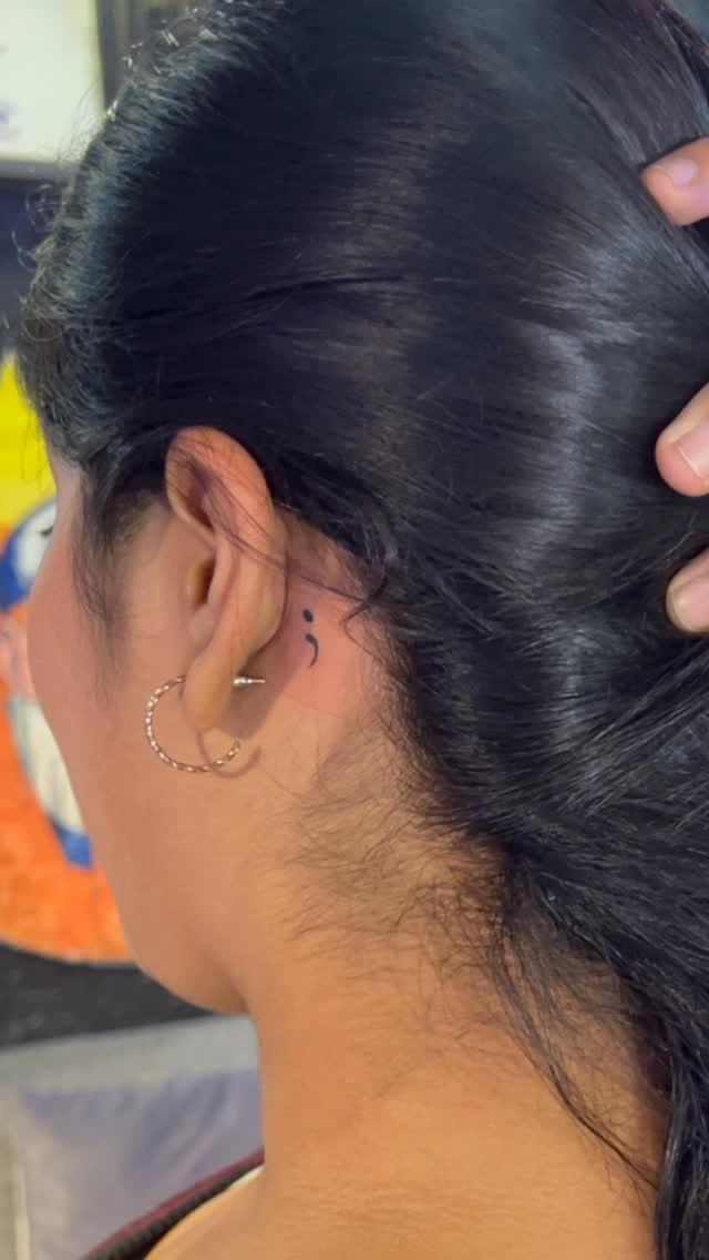 Sick Tattoo Art: 9 Styles That Redefine the Needle 2 A small black semicolon tattoo placed on the skin behind a person's ear.