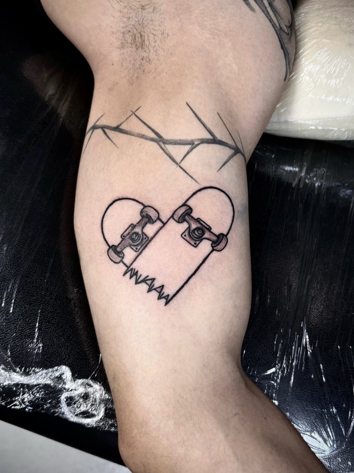 Sick Tattoo Art: 9 Styles That Redefine the Needle 7 A black ink tattoo of a heart-shaped skateboard on a person's leg.