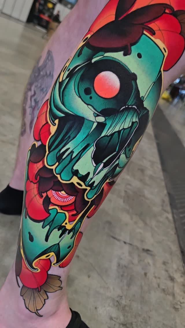 Sick Tattoo Art: 9 Styles That Redefine the Needle 5 A large teal skull tattoo with a red eye and red flowers on a person's leg.