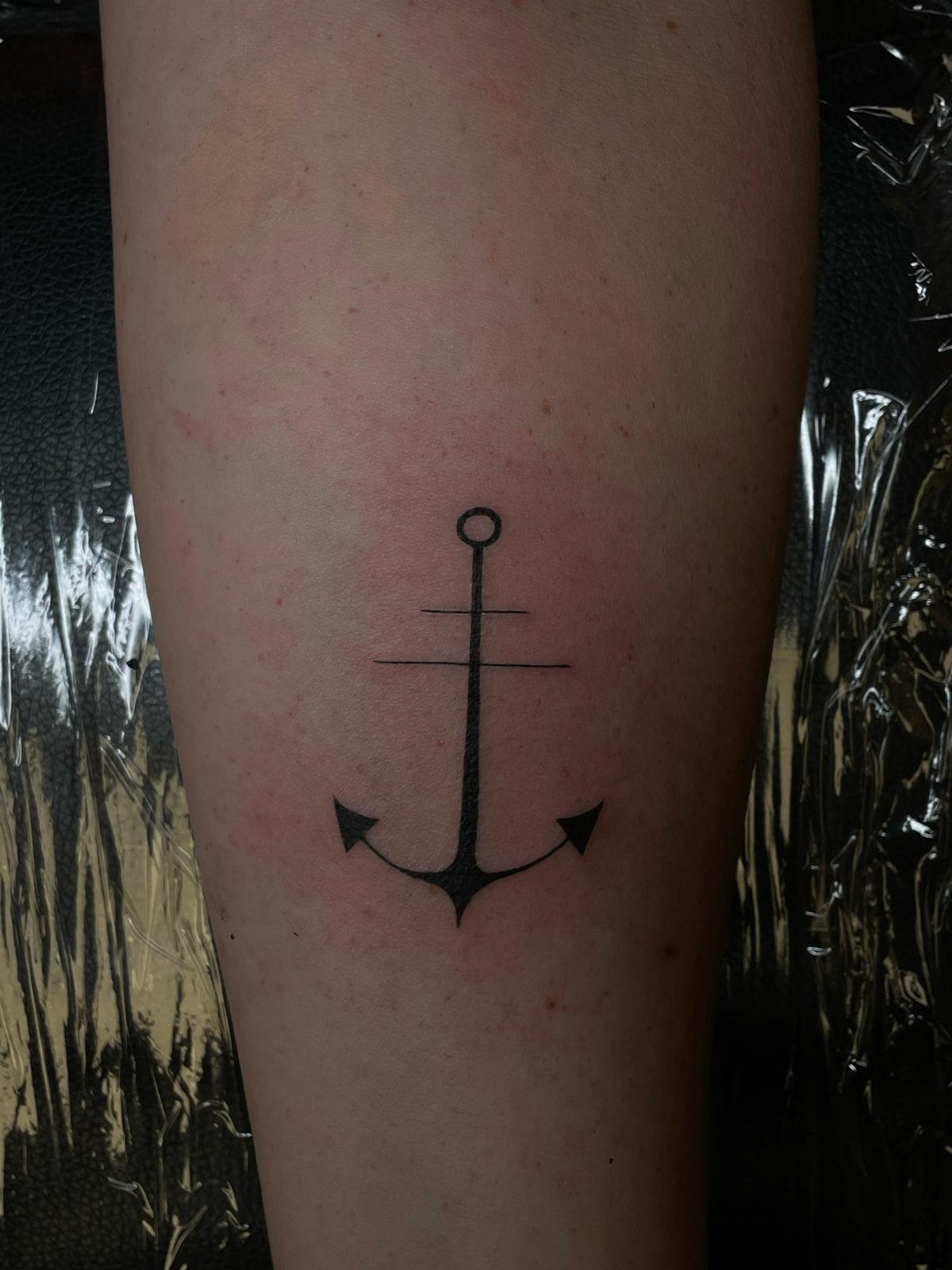 Stencil Tattoo Ideas: 14 Designs for Artists and First-Timers 5 A black ink anchor tattoo on a person's skin against a dark background.