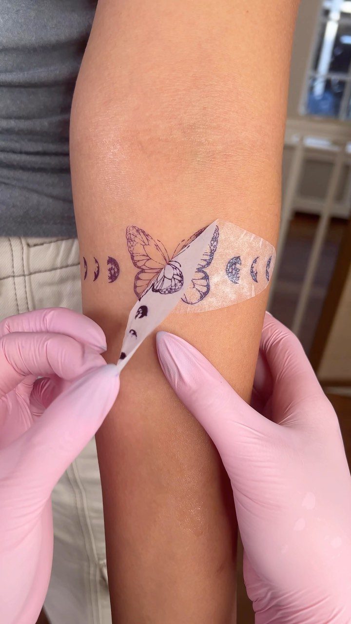 Stencil Tattoo Ideas: 14 Designs for Artists and First-Timers 10 A butterfly and moon phase tattoo stencil being applied to a person's arm.