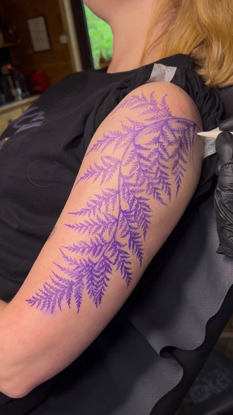 Stencil Tattoo Ideas: 14 Designs for Artists and First-Timers 6 A purple fern leaf stencil applied to a person's arm during a tattoo session.