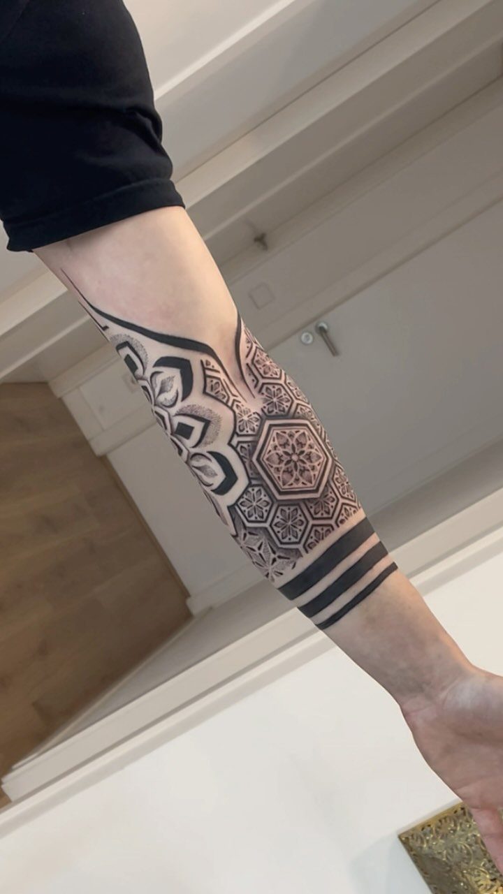 A person's forearm displaying a detailed black ink geometric pattern tattoo with mandala elements.