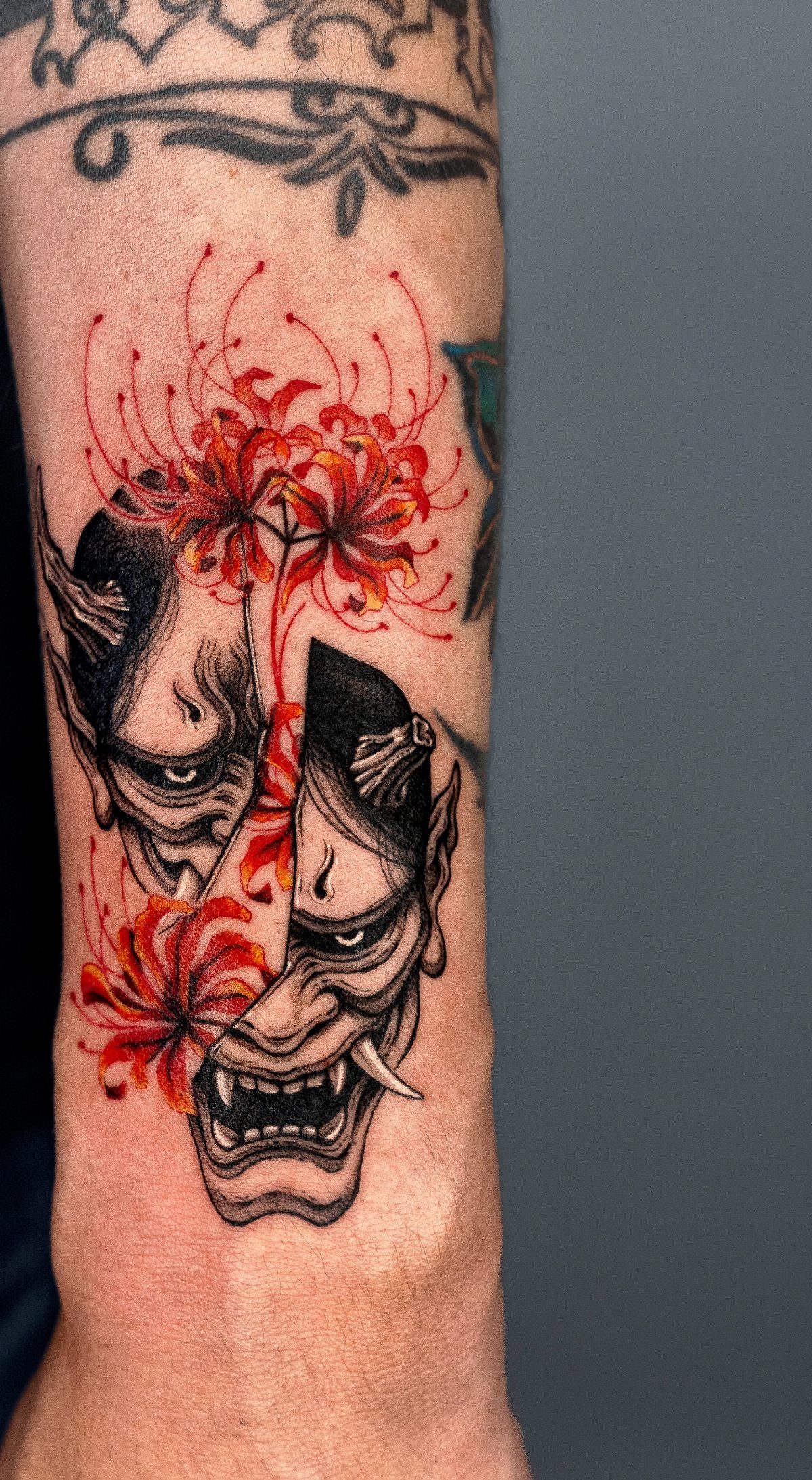 Tattoo Pattern for Beginners: 6 Starter Designs to Trace First 3 Two black and grey demon masks decorated with bright red spider lily flowers tattooed on an arm.