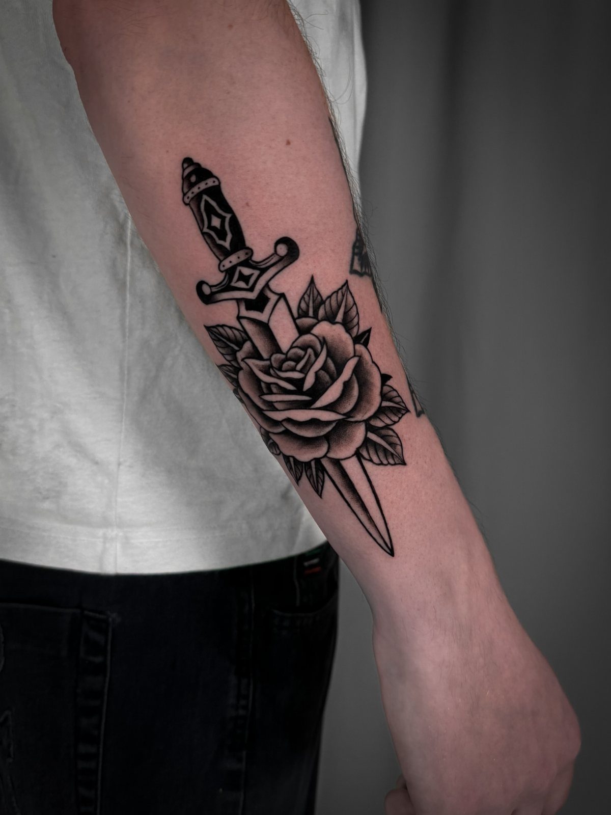 Tattoo Pattern for Beginners: 6 Starter Designs to Trace First 2 A black and grey tattoo of a rose and a dagger on a person's forearm.