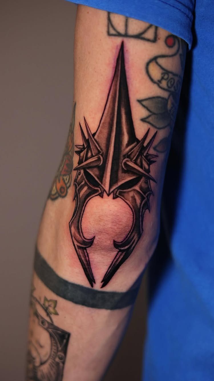 A black and grey spiked helmet tattoo positioned directly over a person's elbow.