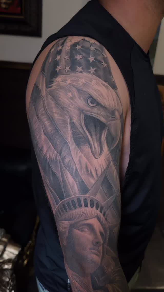 A large black and grey eagle and Statue of Liberty tattoo on a person's outer arm.