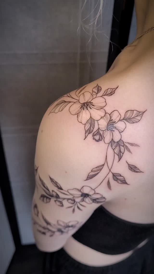 A large black ink floral tattoo covering a person's shoulder and upper arm area.