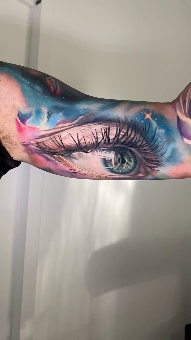 A detailed colorful tattoo of a cosmic eye on a person's upper arm.