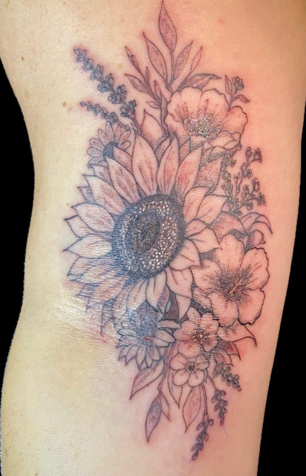 A large black and grey floral tattoo with a central sunflower on a person's skin.