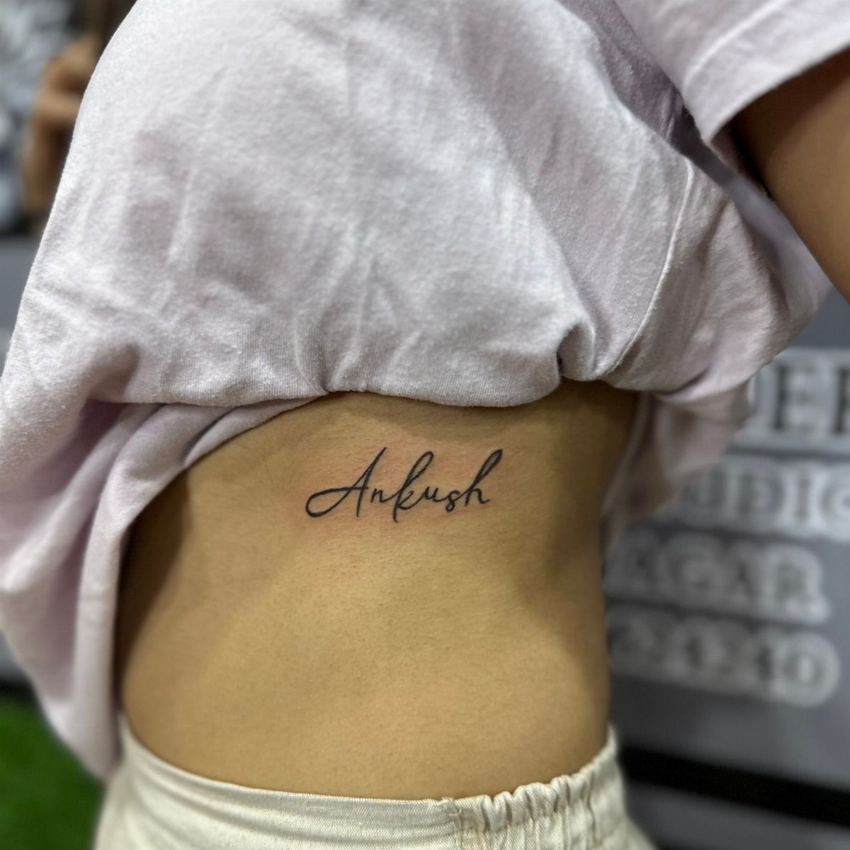 A cursive name tattoo reading Ankush on a person's ribcage side.