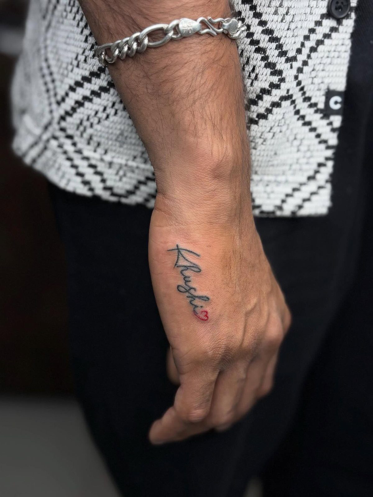 A small cursive name tattoo located on the side of a person's hand.