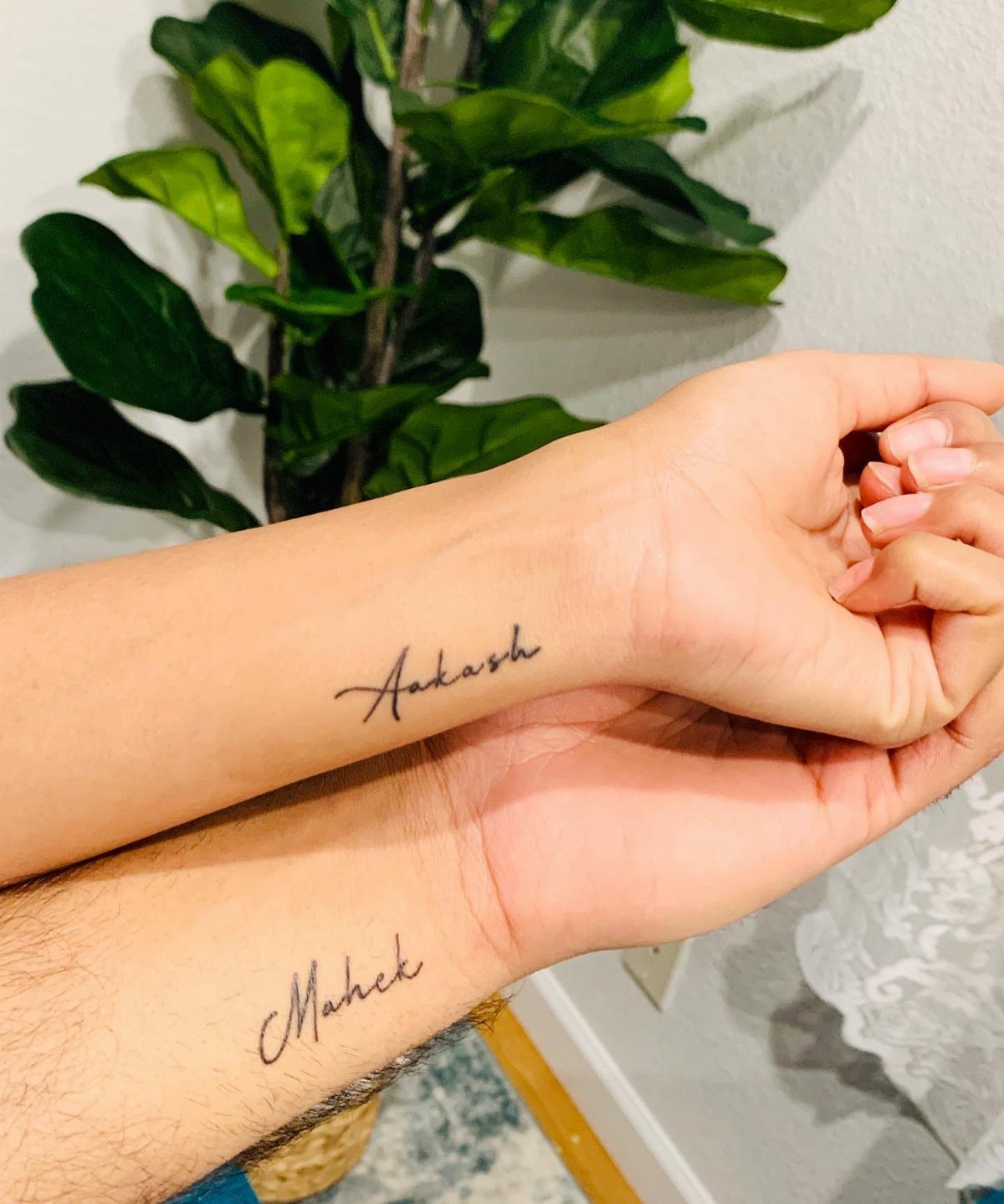Two wrists held together showing small cursive name tattoos on the inner wrist area.