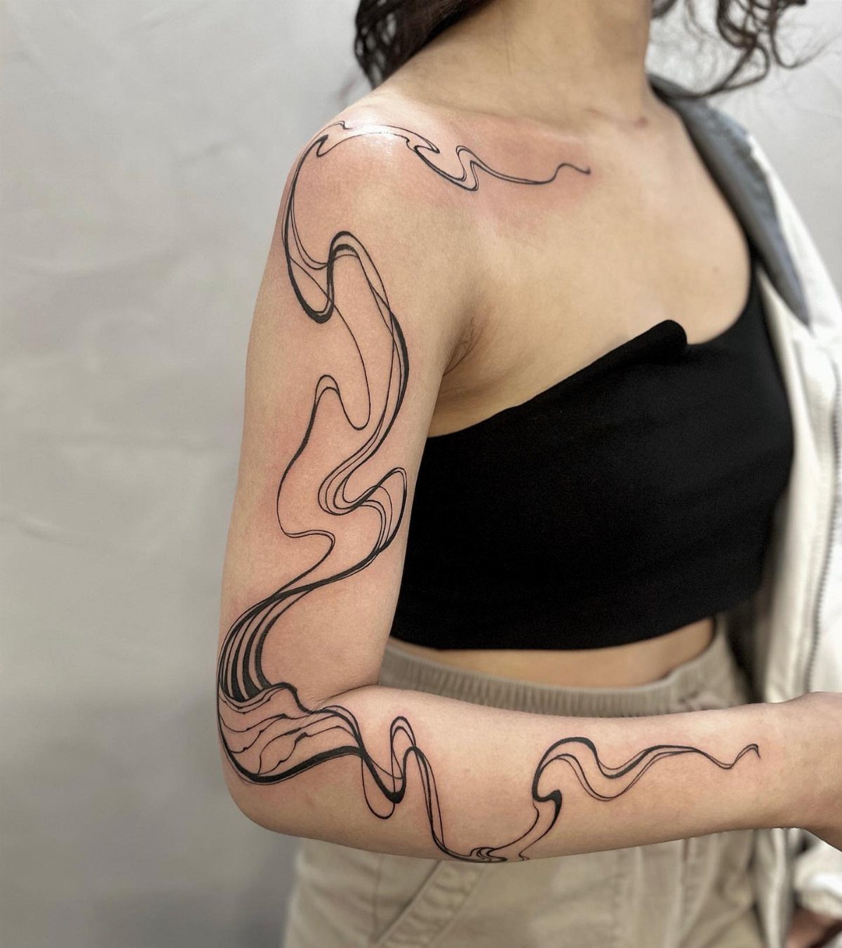 Tattoo Style Drawings: 6 Sketches Worth Keeping in Your Book 2 A person's arm displaying a large, flowing black line art tattoo with abstract wavy patterns.
