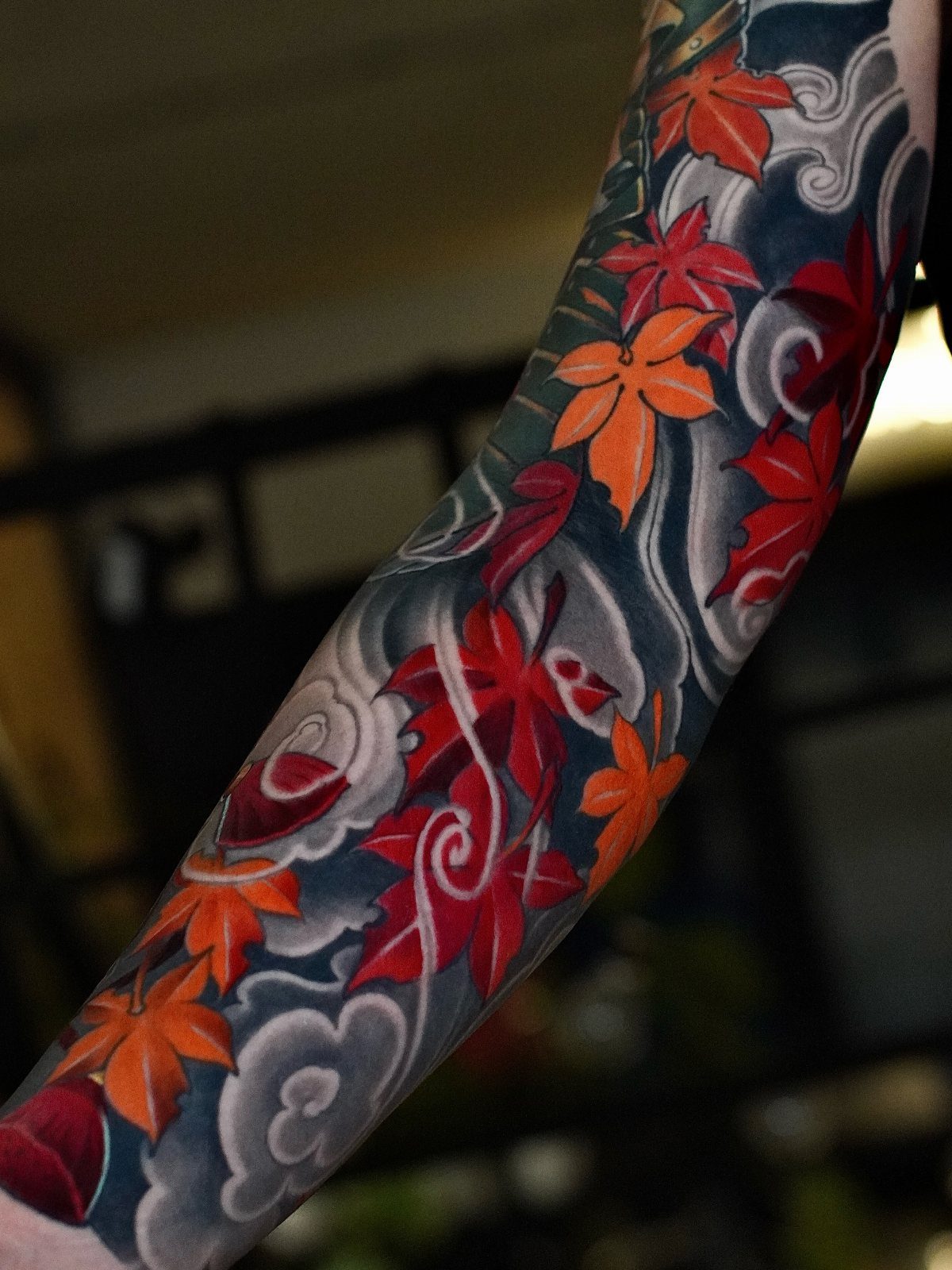 10 Tattoo Style Nature Ideas for Your Next Session 6 A detailed tattoo of vibrant red and orange maple leaves on a person's arm.