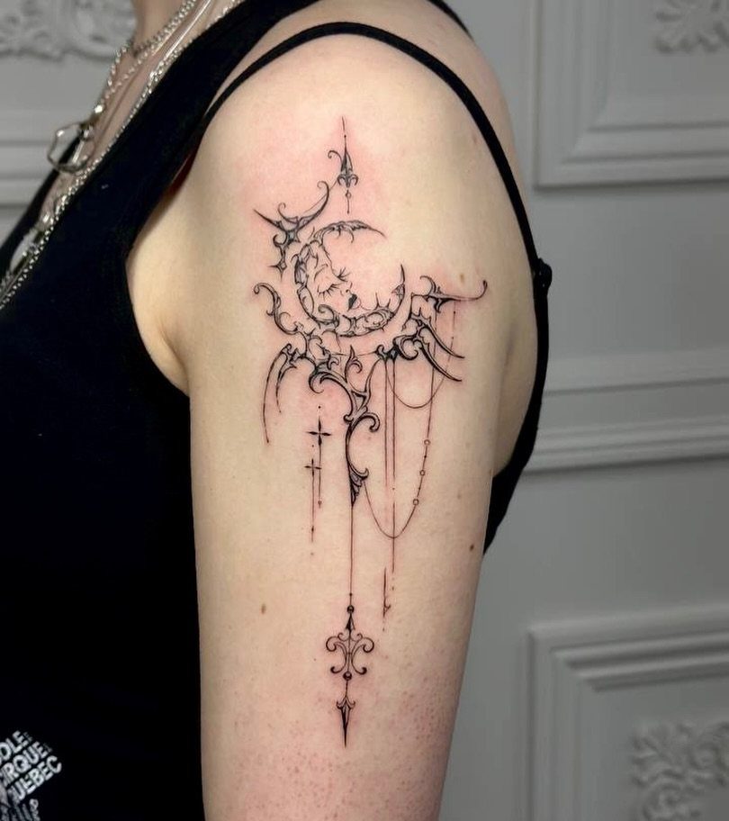 10 Tattoo Style Nature Ideas for Your Next Session 3 A fine line black ink tattoo of a crescent moon with ornate filigree on a person's arm.