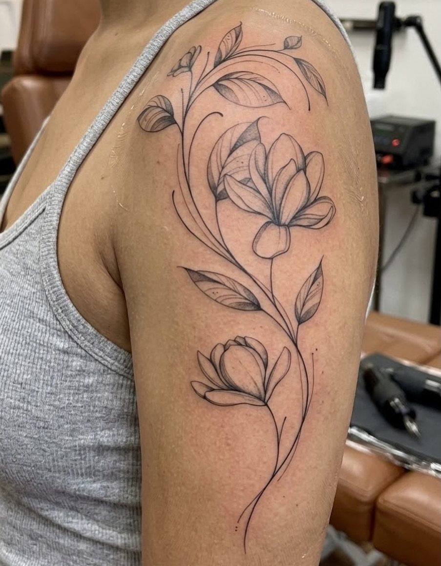 10 Tattoo Style Nature Ideas for Your Next Session 8 A fine line floral tattoo with magnolia flowers and leaves on a person's upper arm.