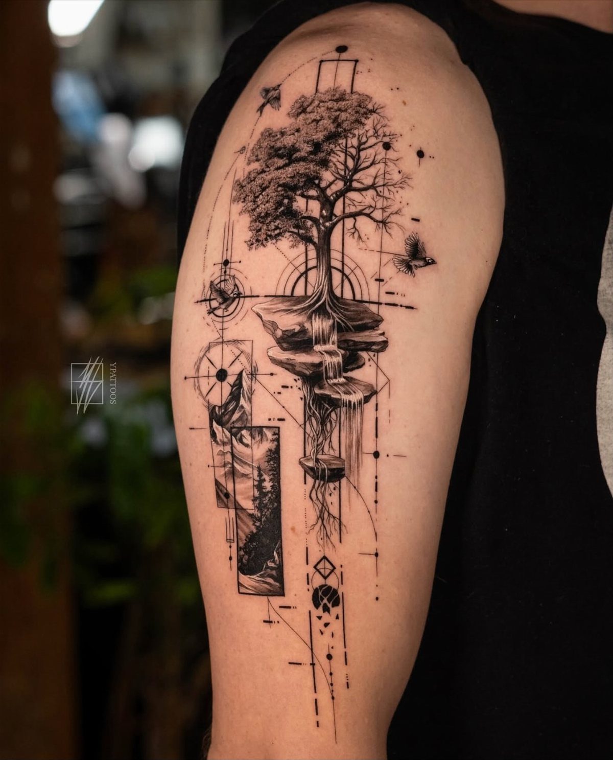 10 Tattoo Style Nature Ideas for Your Next Session 7 A detailed black ink tree tattoo with a waterfall and geometric lines on a person's arm.