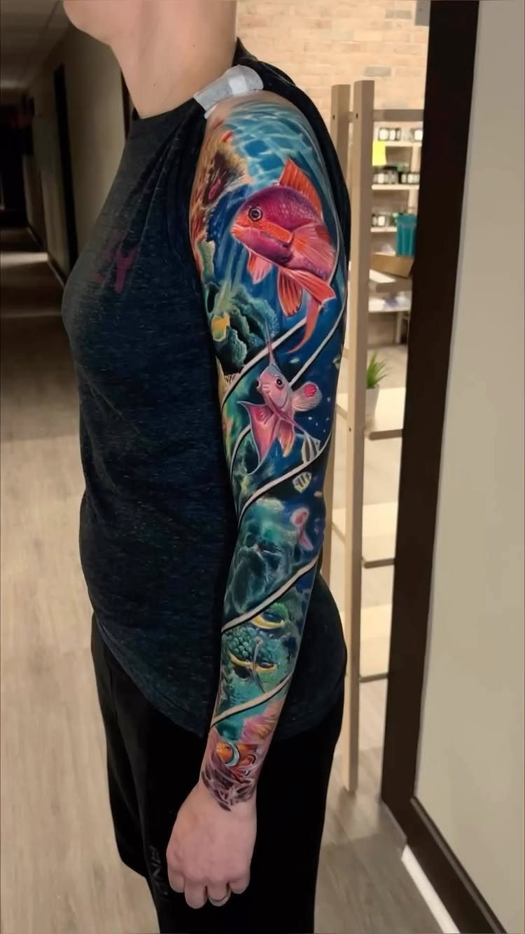 10 Tattoo Style Nature Ideas for Your Next Session 10 A person's arm displaying a colorful underwater sleeve tattoo with pink fish and blue waves.