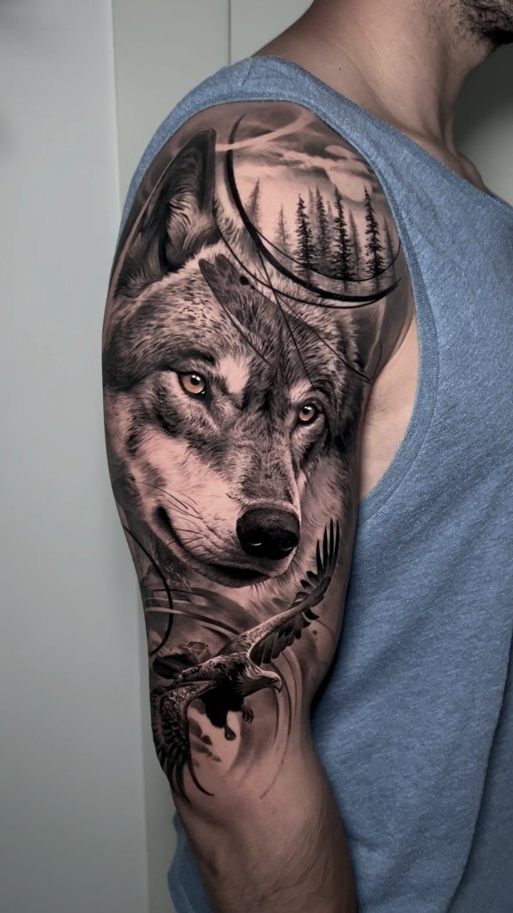 10 Tattoo Style Nature Ideas for Your Next Session 1 A detailed black and grey wolf tattoo on a man's shoulder with forest and eagle elements.