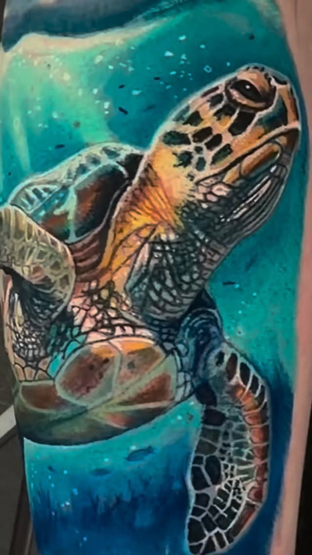 A colorful sea turtle tattoo swimming through vibrant blue and turquoise ocean water.